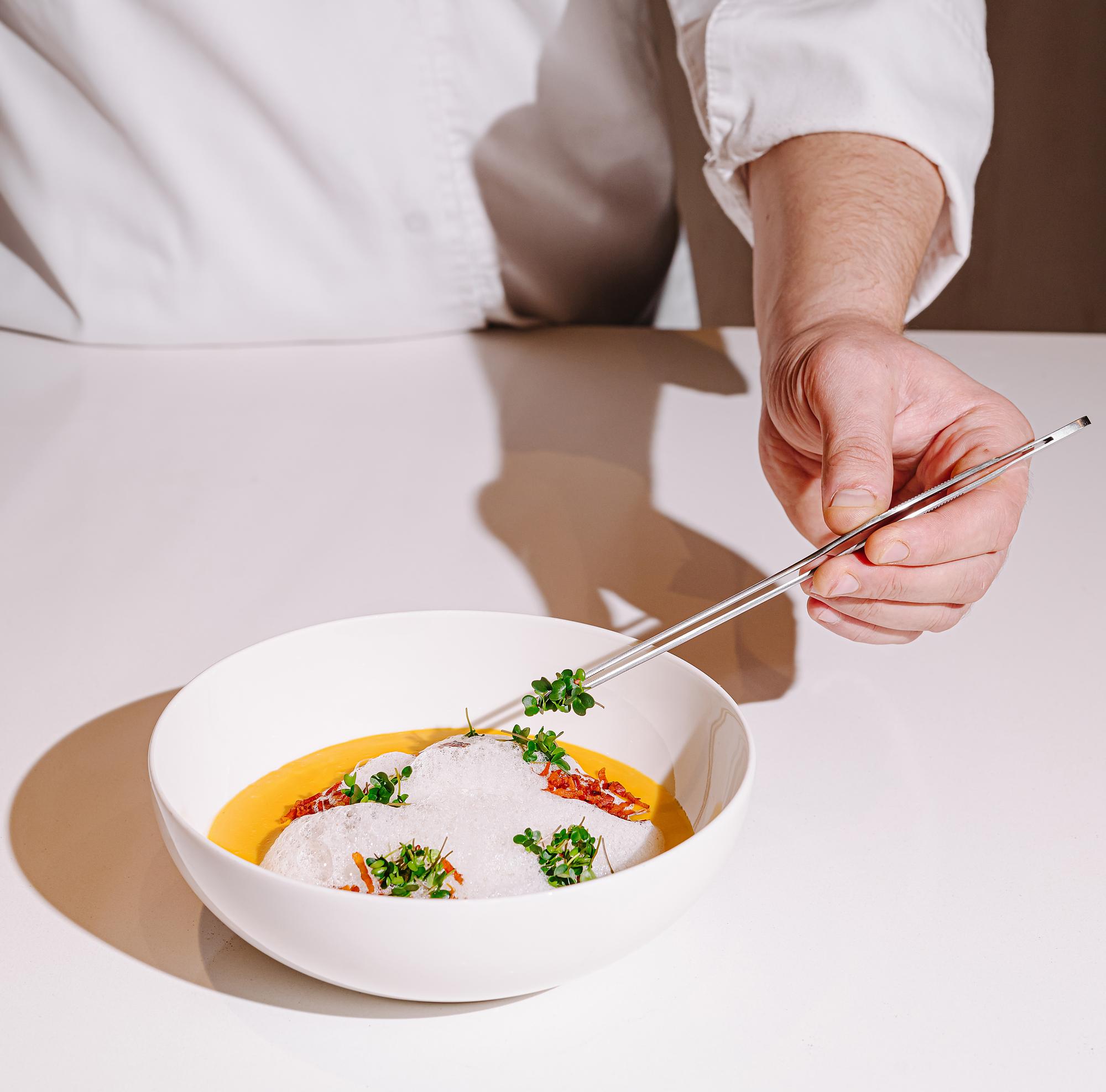 Chef plating a warm bowl on a wooden table